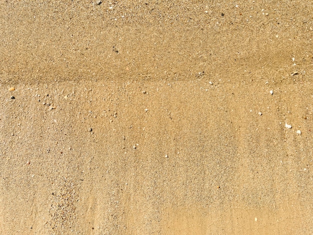 Een achtergrond van kleine zandsteentjes en vloeiende golven op het strand Zomervakantieconcept