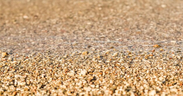 Een achtergrond van kleine zandsteentjes en vloeiende golven op het strand Zomervakantieconcept