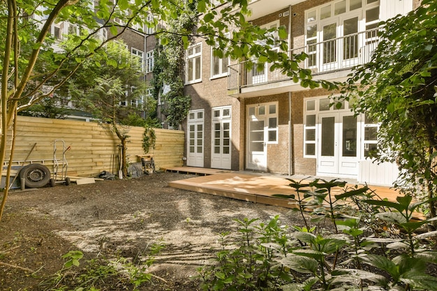 Een achtertuin met enkele bomen op de achtergrond en een houten terras op de grond omringd door struiken en planten