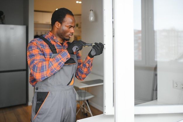 een Afrikaanse reparateur repareert of installeert metaalplastische ramen in het appartement