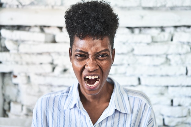 Een Afrikaanse vrouw zit op haar bank en schreeuwt erg boos en agressief.