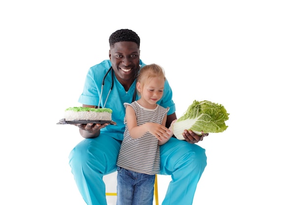 Een Afro-Amerikaanse arts vertelt een jong kind over gezonde en goede voeding terwijl hij een cake en kool in zijn hand houdt. Het concept van gezond eten