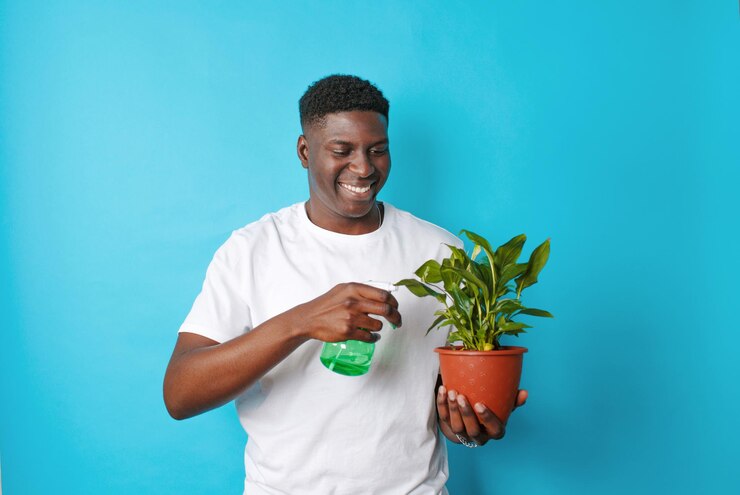 Een Afro-Amerikaanse man in een wit T-shirt zorgt voor bloemen in een pot op een blauwe achtergrond