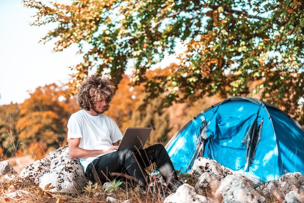 Een afro-man die in de natuur zit en een laptop gebruikt voor een online vergadering tijdens een pandemie van het coronavirus