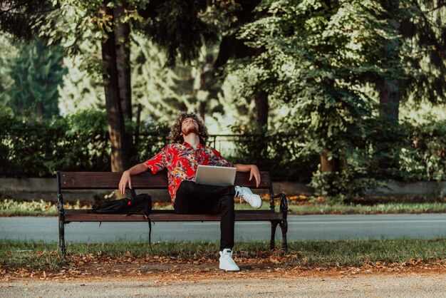 Een Afro-tiener gebruikt een laptop voor een onlinevergadering terwijl hij op een bankje in het park zit