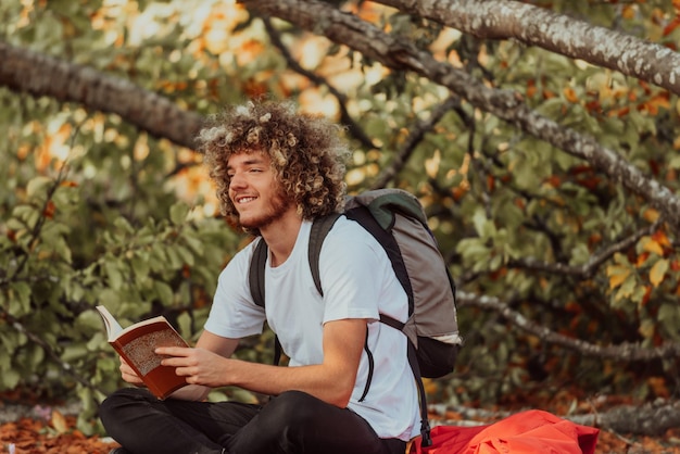 Een Afro-tiener ontspant terwijl hij een boek leest terwijl hij in het bos zit bij prachtig herfstweer