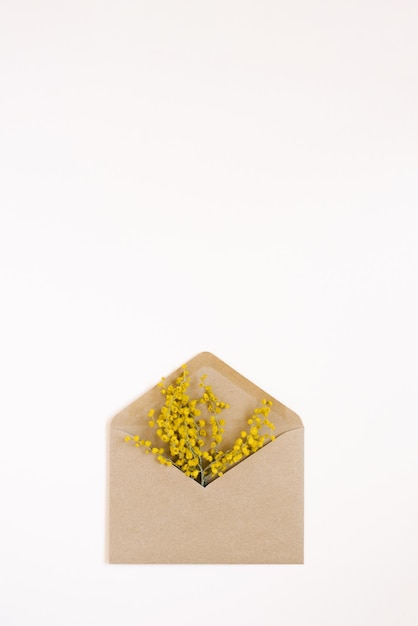 Een ambachtelijke envelop met mimosa bloemen erin op een witte achtergrond Platte lay- en kopieerruimte