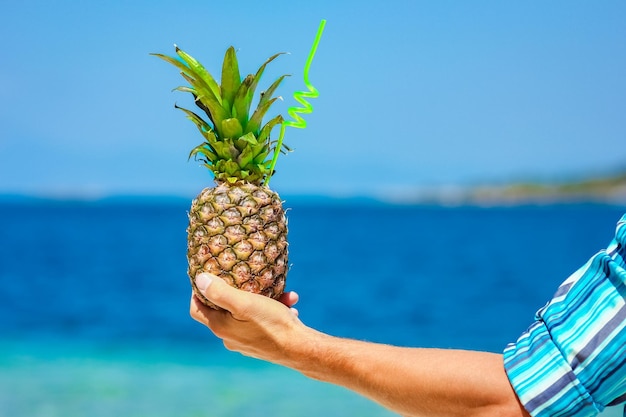Een ananas in de handen van een man aan zee in de natuur op de achtergrond van een reis