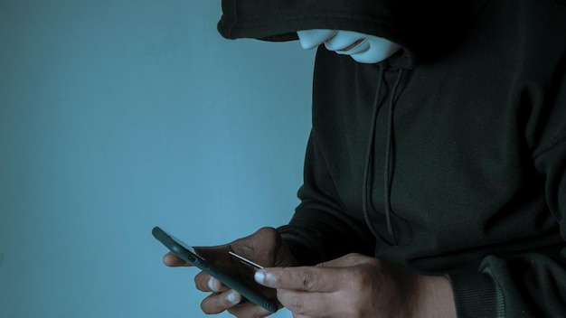 Een anonieme gemaskerde hacker gebruikt een smartphone om financiële creditcardgegevens binnen te dringen Hacking- en malwareconcept