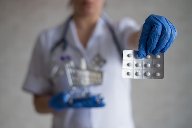 Een anonieme vrouwelijke arts in rubberen handschoenen toont een blisterverpakking met pillen en houdt een mini-winkelwagentje vast met een volledig pakket verschillende medicijnen Aanbevelingen van apothekers