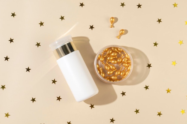 Een anti-aging serum of etherische olie in gouden capsules als cadeau voor kerstvakantie liggend op een beige achtergrond met confetti eromheen