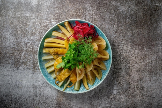 Een aperitief in een restaurant, een assortiment van ingemaakte groenten van komkommer, tomaat en peper. Gesneden augurken in lagen op een bord met groen tegen een grijze stenen tafel