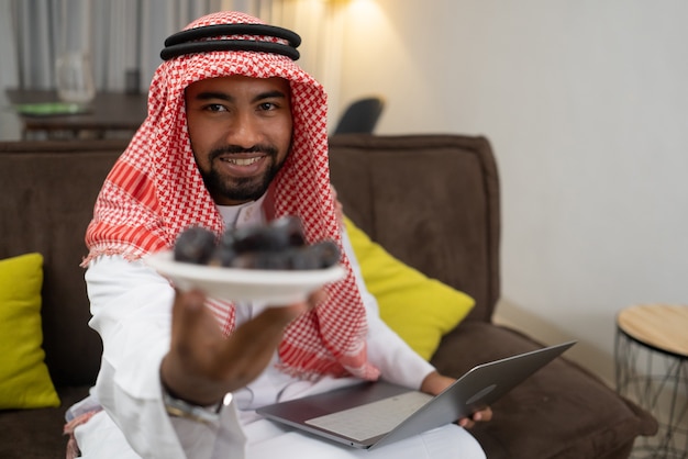 Een Arabische zakenman die een tulband draagt en een bord met dadels draagt terwijl hij op het werk zit