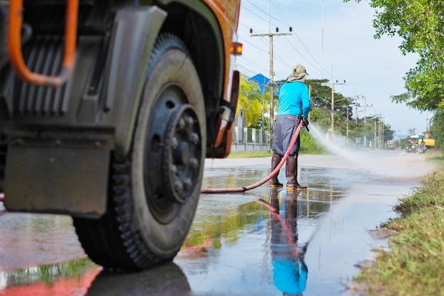 Een arbeider die water bespuit om de weg schoon te maken met water onder druk, natte reiniging van straat.