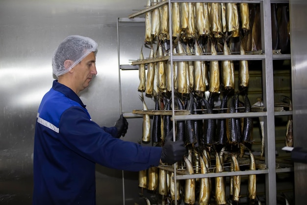 Een arbeider duwt een kar met gerookte vis in een industriële oven