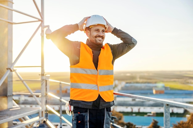 Een arbeider in de zware industrie die een helm op het hoofd zet terwijl hij op hoogte staat