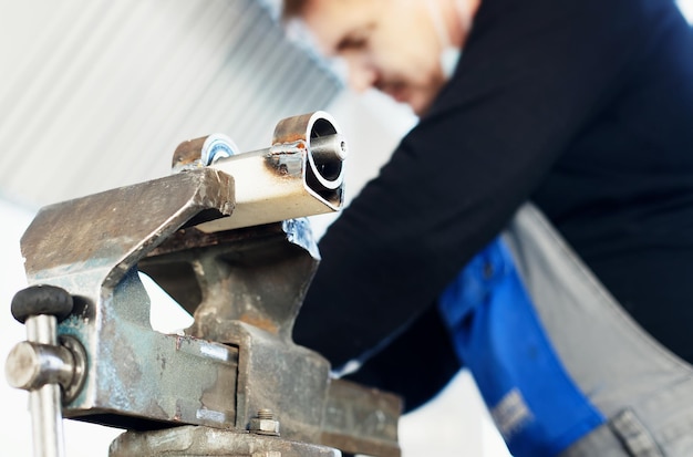 Een arbeider in overall werkt achter een werkbank met metalen bankschroeven Productie van metalen onderdelen in de fabriek