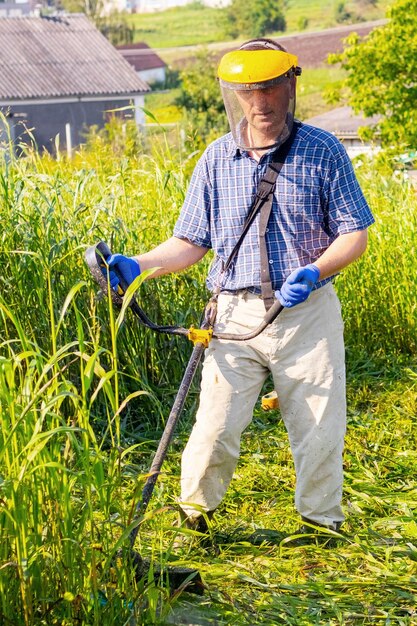 Een arbeider maait hoog gras met een elektrische trimmer