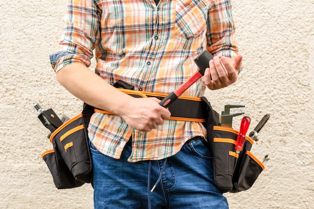 Een arbeider met gereedschapstassen aan zijn riem en een rubberen hamer in zijn hand.