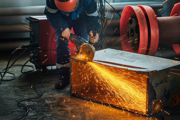 Een arbeider snijdt metaal met een handslijper in de productieruimte en er vliegen heldere vonken uit Een echte werkomgeving