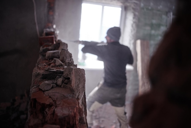 Een arbeidersarbeider breekt een bakstenen muur met een jackhammer, bouwt en repareert zijn huis.