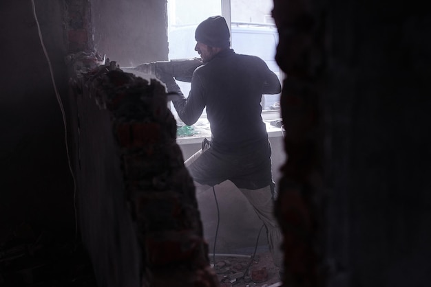 Een arbeidersarbeider breekt een bakstenen muur met een jackhammer, bouwt en repareert zijn huis.