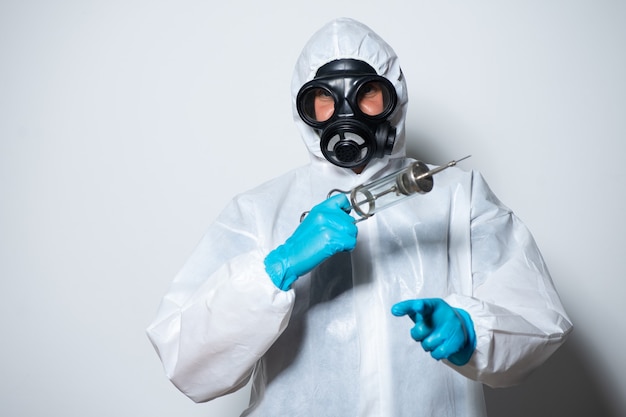Een arts die een beschermingspak draagt met een gasmasker tegen COVID-19 (Coronavirus) met spuit en vaccin op witte achtergrond