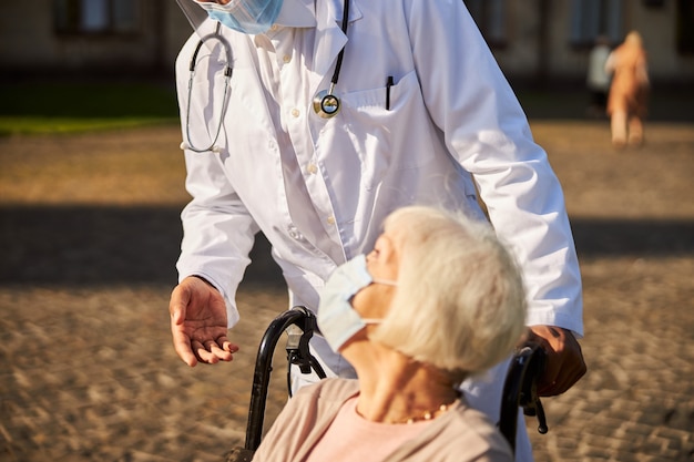 een arts die leunt tegen een oude dame met een masker in een rolstoel