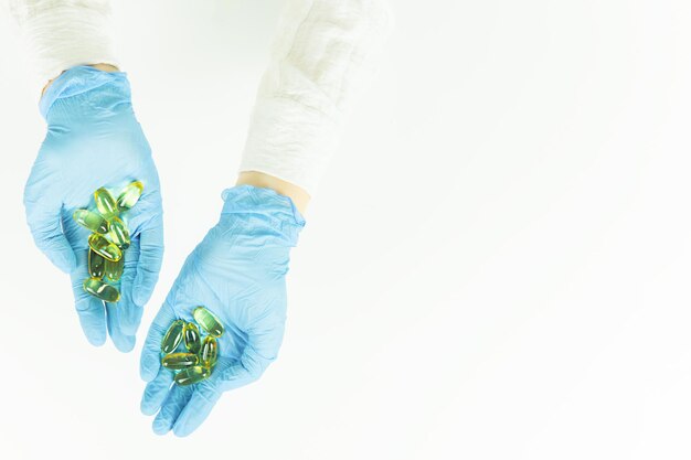 Een arts in blauwe medische handschoenen houdt gele pillen in capsules