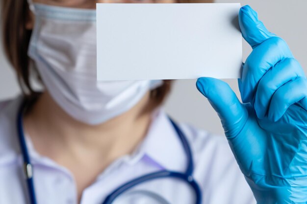 Een arts met blauwe medische handschoenen houdt een visitekaartje voor zich Closeup achtergrond met kopieerruimte Leeg visitekaartjes voor tekst