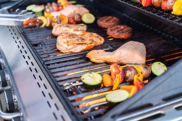 Een Atlantische zalm, kipfilet, groentespiesjes en vegetarische burgers grillen op een buitengrill.