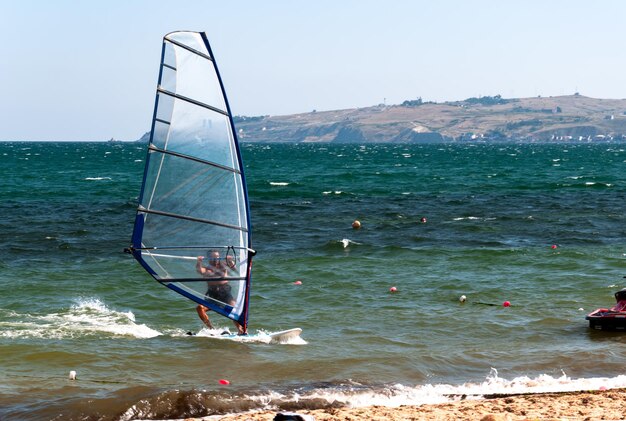 Een atleet die een windsurfer bestuurt, zwemt naar de kust