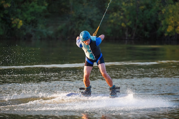 Een atleet doet een truc op het water Een renner springt op een wakeboard tegen een achtergrond van een groen bos Zonsondergang op het meer