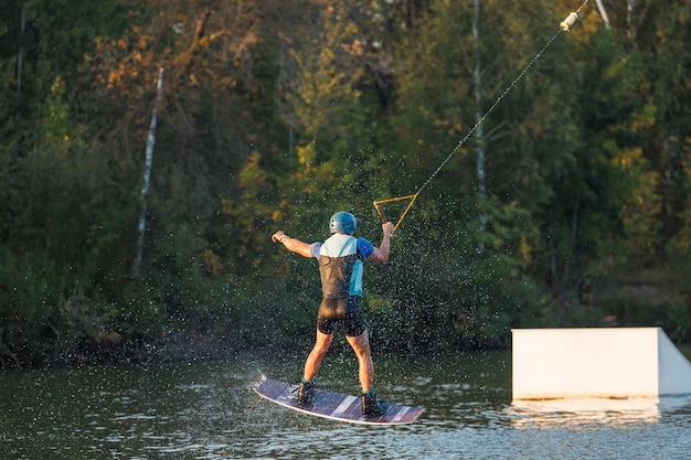 Een atleet springt over het water Wakeboardpark bij zonsondergang Ruiter voert een truc uit op het bord