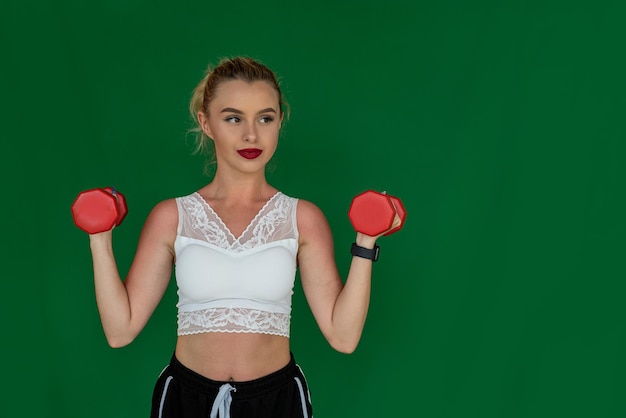 Een atletische, goed verzorgde vrouw met een schattig uiterlijk staat met halters op een effen achtergrond