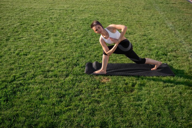 Een atletische jonge vrouw met een lichte huid en een atletisch postuur beoefent yoga in het park. Het concept van gezond leven, zelfzorg en welzijn. Gedraaide Zijhoek Pose. Parivritta parshvakonasana.