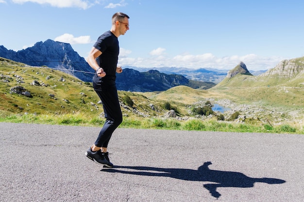 Een atletische man sport buiten Een man springt aan een touw tegen de achtergrond van een berglandschap