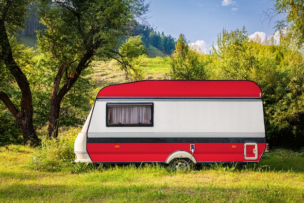 Een auto-aanhangwagen, een camper, geschilderd in de nationale vlag van oostenrijk, staat geparkeerd in een bergachtige.