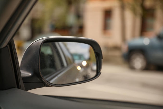 Een auto is zichtbaar door een zijspiegel met een groene auto op de achtergrond.