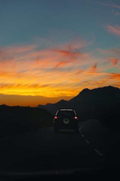 Foto een auto rijdt over een weg met daarachter de ondergaande zon