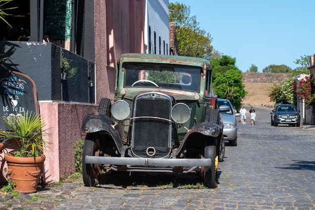 Een auto staat geparkeerd op een geplaveide straat met een bakstenen muur en een gebouw op de achtergrond.