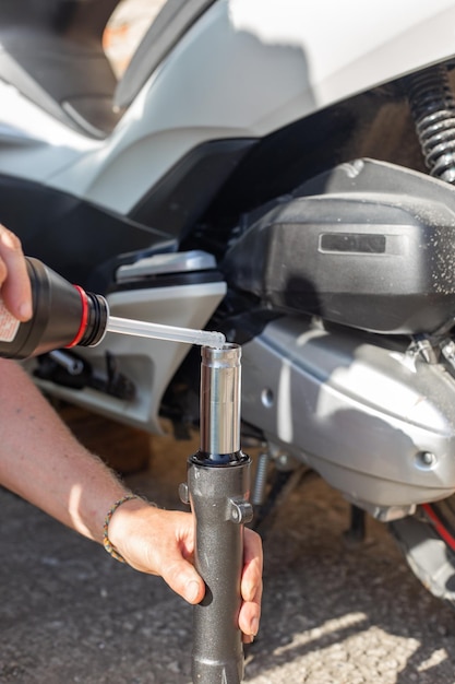 Een automonteur repareert een motorfiets Een man giet olie in de schokdemper van de voorvork van een scooter