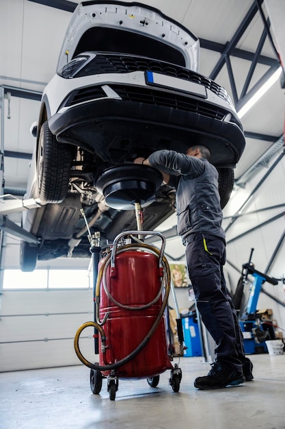 Een automonteur staat onder de auto en ververst de motorolie erop