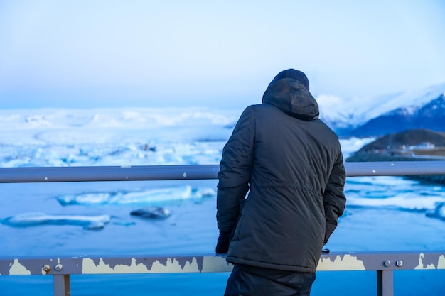 Een avontuurlijke jonge man op de brug die in de winter naar het Jokulsarlonmeer in IJsland kijkt