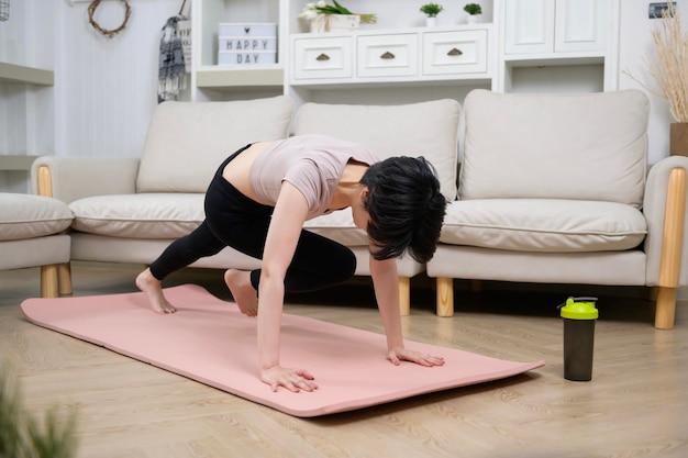 Een Aziatische jonge vrouw is aan het trainen op een fitnessmat om thuis een gezond levensstijlconcept uit te oefenen