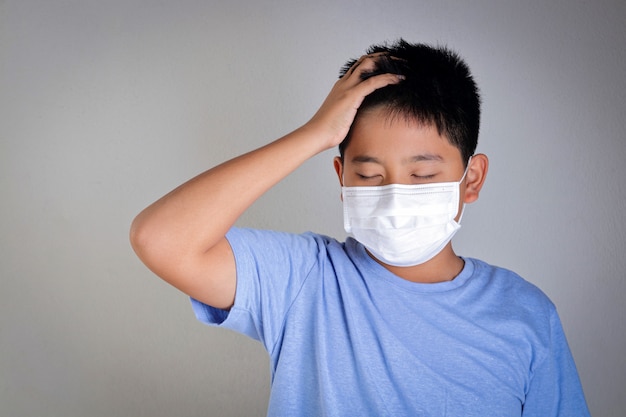 Een Aziatische jongen draagt een masker dat zijn mond en neus bedekt en coronavirus of COVID-19 voorkomt. Gezondheid van kinderen concept