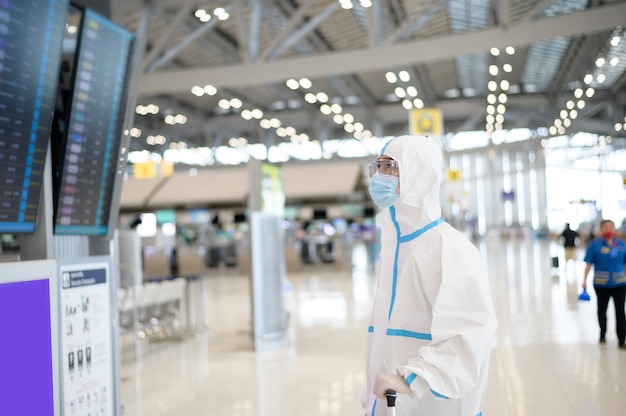 Een Aziatische man draagt een pbm-pak op de internationale luchthaven, veiligheidsreizen, covid-19-bescherming, sociaal afstandsconcept.