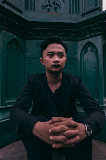 Foto een aziatische man in een zwart pak zit alleen voor het enge grafmonument