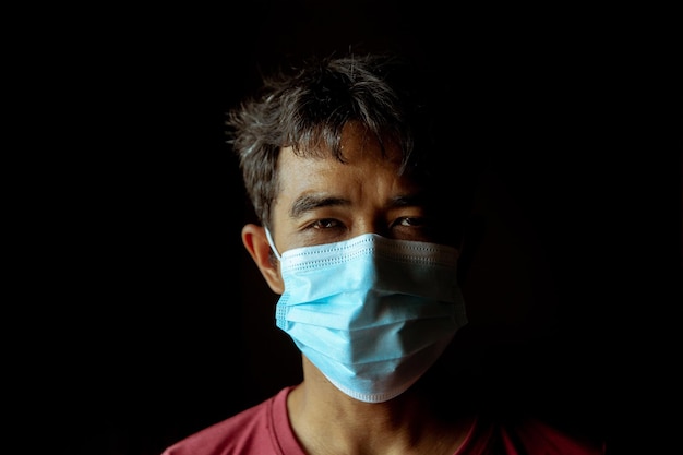Een Aziatische mannelijke patiënt die een masker draagt, ziet er moe uit in het donker