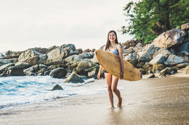 Een Aziatische sexy jonge vrouw die op strand met surfplank in Phuket Thailand loopt